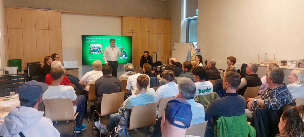 Helferinnen und Helfer im TSV-Konferenzraum, Robert Langwieser vor dem Hintergrund der Präsentation beim Beantworten der Fragen